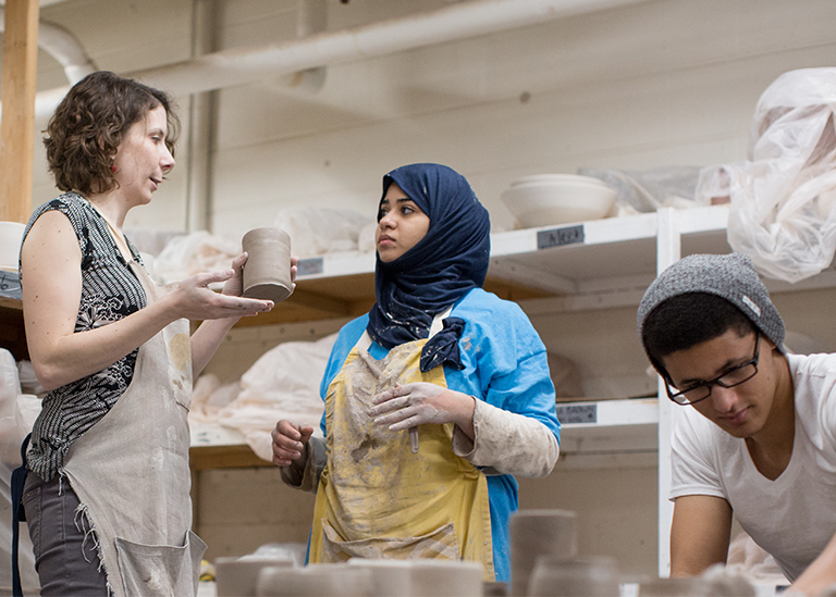 a teacher holds a clay pot in a studio with a woman wearing a head scarf