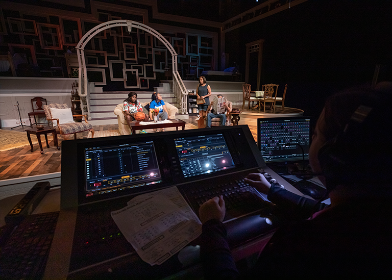 a group of actors stand on a stage performing and you see a production in the background